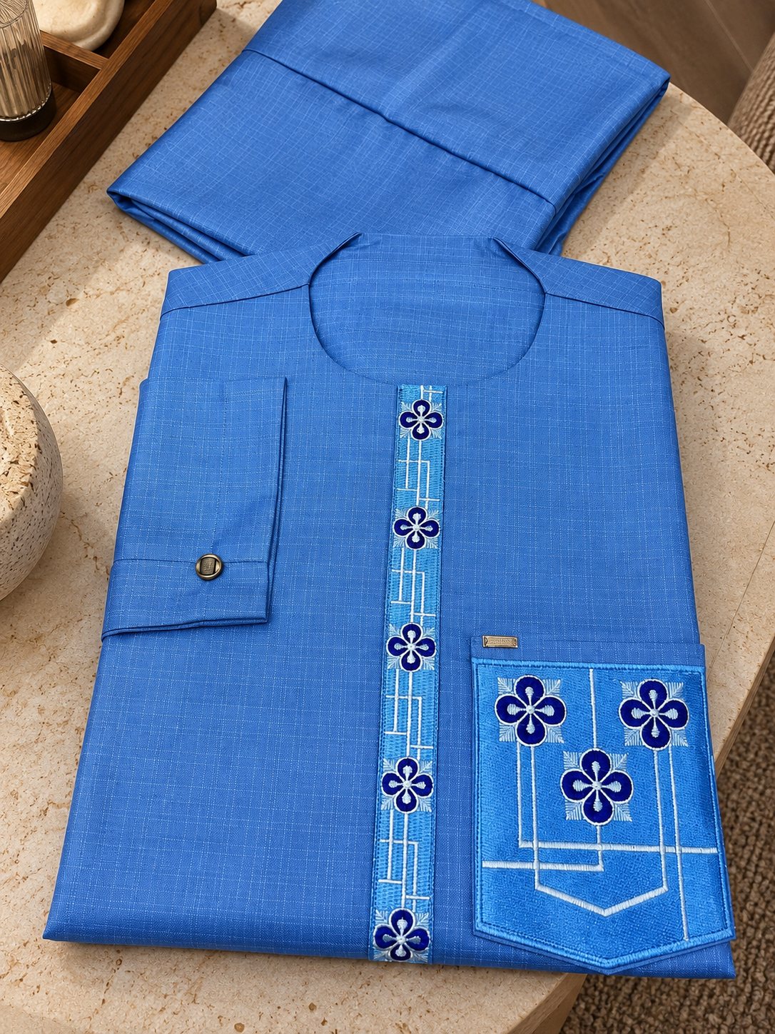Bleu soutenu, fleurs brodées bleu roi le long du plastron et sur la poche. La broderie du Cascade, dans un bleu plus intense.