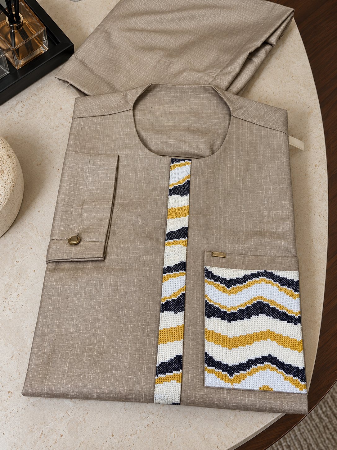 Ensemble taupe plié, vagues brodées bleu nuit, jaune et blanc sur le plastron et la poche